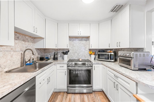 kitchen featuring sink, stainless steel appliances, backsplash, white cabinets, and light wood-type flooring