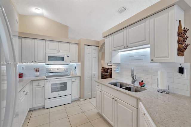 kitchen with light tile patterned flooring, sink, white cabinetry, vaulted ceiling, and white appliances