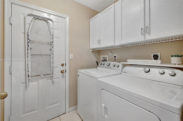 laundry room with cabinets, washing machine and clothes dryer, a textured ceiling, and light tile patterned floors