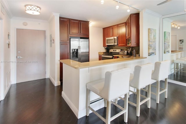 kitchen with dark hardwood / wood-style floors, kitchen peninsula, crown molding, a breakfast bar area, and appliances with stainless steel finishes