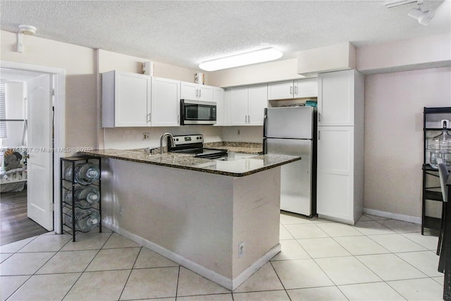 kitchen with kitchen peninsula, dark stone countertops, appliances with stainless steel finishes, light tile patterned flooring, and white cabinetry