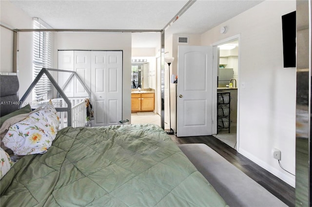 bedroom featuring stainless steel refrigerator, ensuite bathroom, a textured ceiling, a closet, and hardwood / wood-style flooring