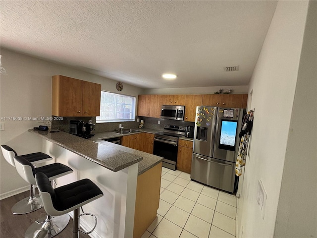 kitchen featuring a breakfast bar, sink, light tile patterned floors, appliances with stainless steel finishes, and kitchen peninsula