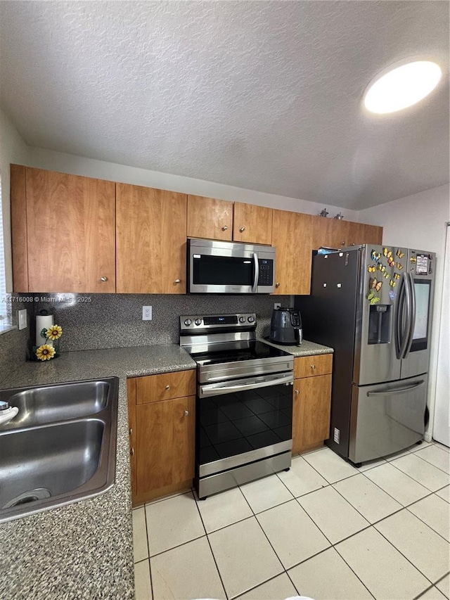 kitchen featuring appliances with stainless steel finishes, sink, light tile patterned floors, a textured ceiling, and decorative backsplash