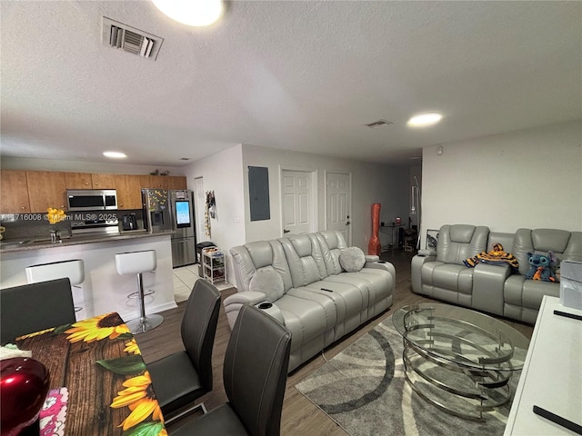 living room featuring a textured ceiling, electric panel, and light hardwood / wood-style floors