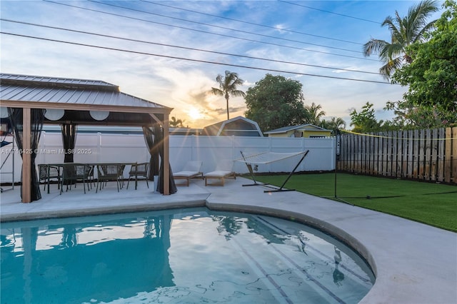 pool at dusk featuring a gazebo and a lawn