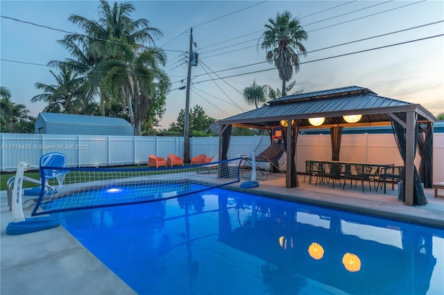 pool at dusk featuring a gazebo and a patio area