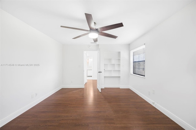 spare room with built in shelves, dark hardwood / wood-style floors, and ceiling fan