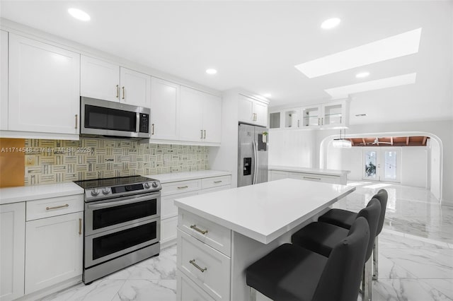 kitchen featuring a breakfast bar, a center island, decorative backsplash, appliances with stainless steel finishes, and white cabinetry