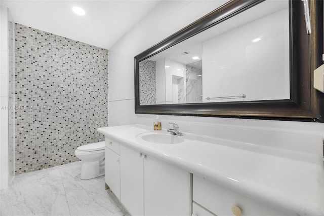 bathroom with a shower, vanity, tile walls, and toilet