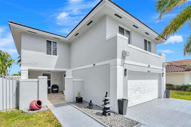 view of front of house with stucco siding, decorative driveway, a garage, and fence