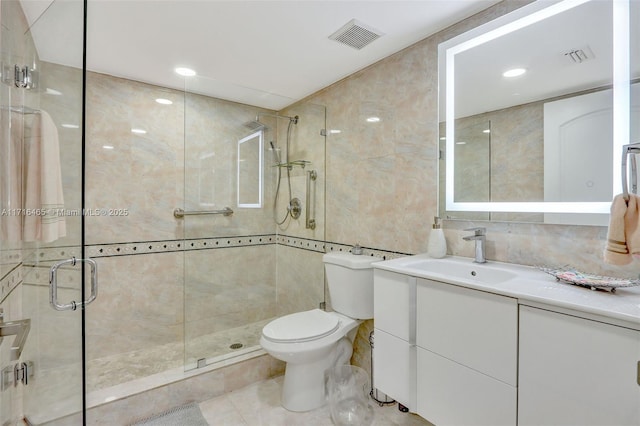 full bath featuring visible vents, toilet, vanity, a stall shower, and tile walls