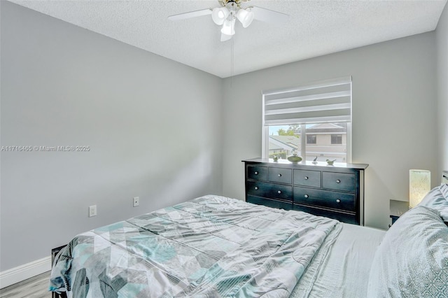 bedroom featuring a textured ceiling, a ceiling fan, baseboards, and wood finished floors