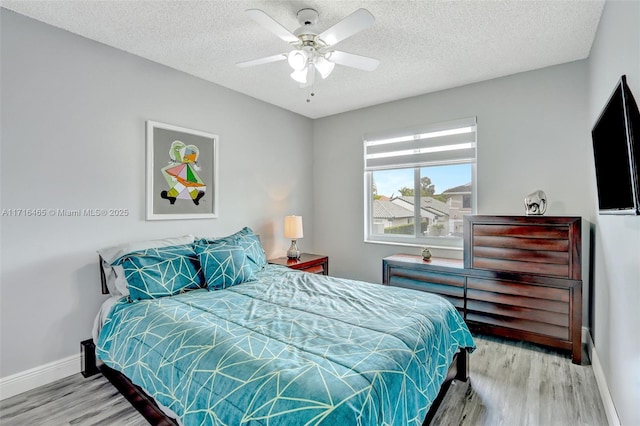 bedroom featuring ceiling fan, a textured ceiling, baseboards, and wood finished floors