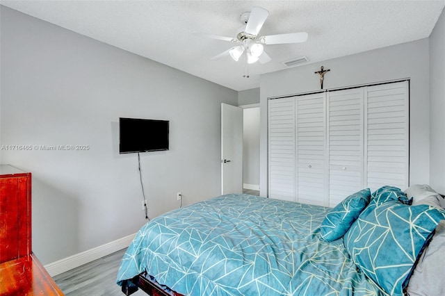 bedroom with visible vents, baseboards, wood finished floors, a closet, and a textured ceiling