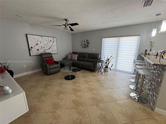 living room with ceiling fan, light tile patterned flooring, and a textured ceiling