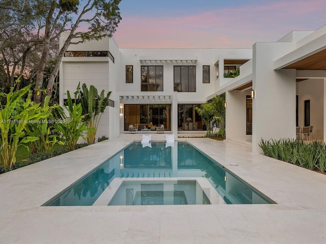 back house at dusk with a swimming pool with hot tub and a patio area