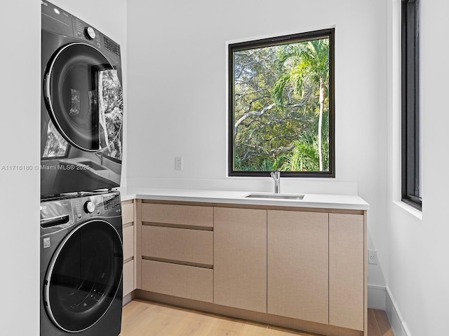 laundry area featuring stacked washer and clothes dryer, cabinet space, light wood-style floors, a sink, and baseboards