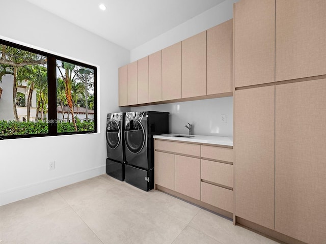 clothes washing area with light tile patterned floors, washing machine and dryer, a sink, baseboards, and cabinet space