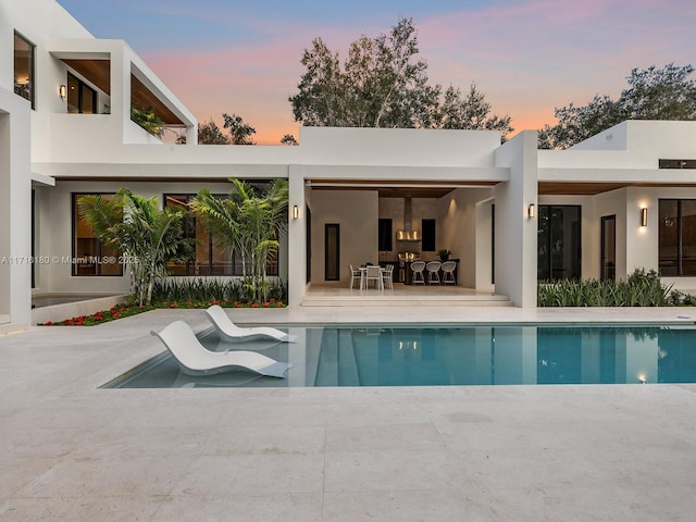 rear view of house with stucco siding, an outdoor pool, and a patio