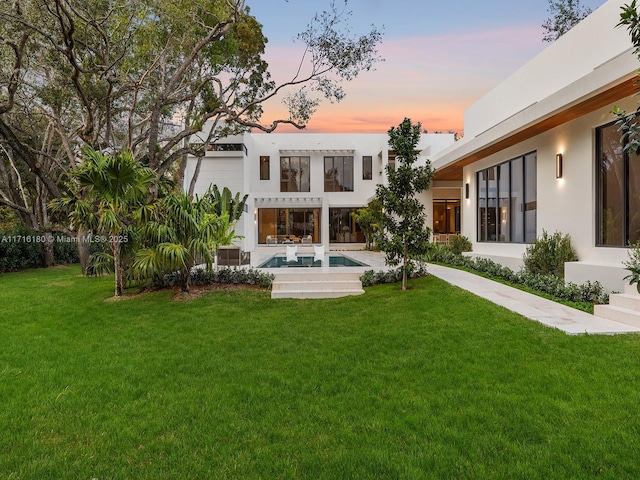 back of property featuring an outdoor pool, a yard, and stucco siding