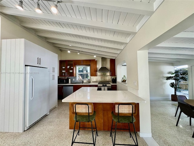 kitchen with stainless steel appliances, wall chimney range hood, vaulted ceiling with beams, kitchen peninsula, and a breakfast bar