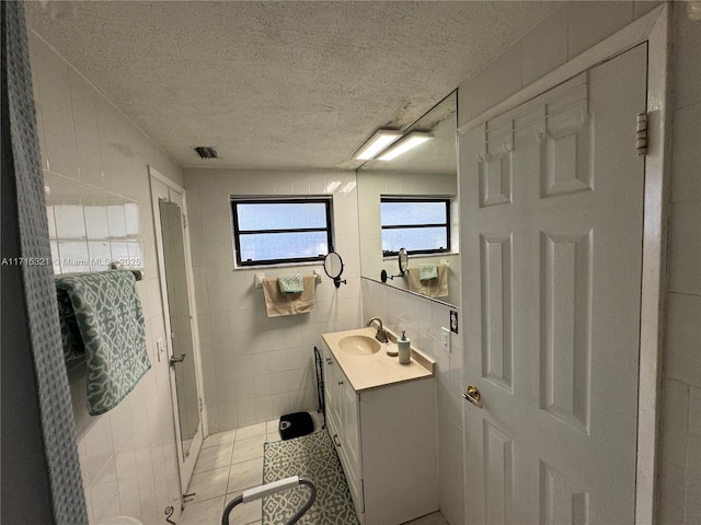 bathroom with tile patterned floors, a textured ceiling, vanity, and tile walls