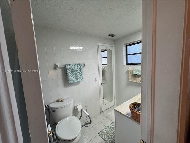 bathroom featuring tile patterned floors, toilet, tile walls, a textured ceiling, and vanity