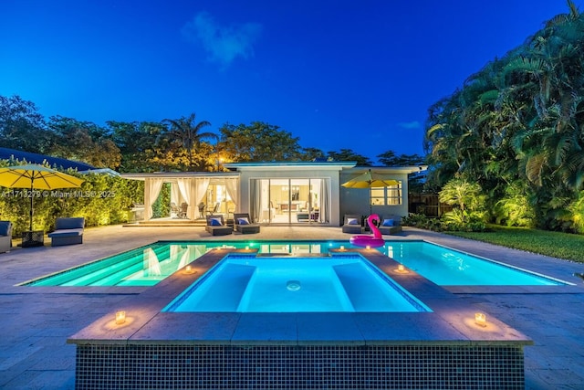 pool at twilight with an in ground hot tub and a patio area