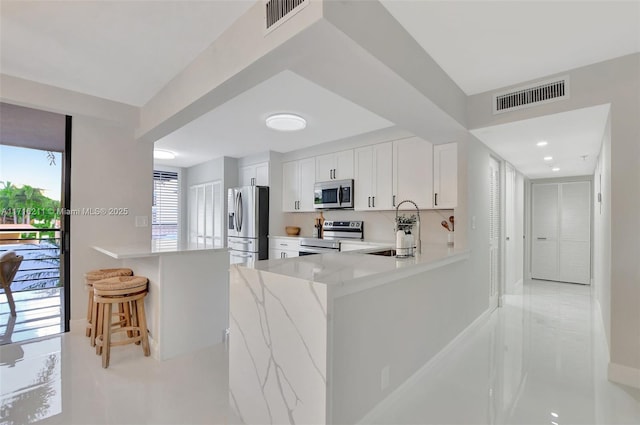 kitchen with sink, stainless steel appliances, kitchen peninsula, a kitchen bar, and white cabinets