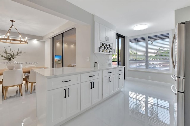 kitchen featuring stainless steel refrigerator, light stone countertops, white cabinetry, hanging light fixtures, and tasteful backsplash