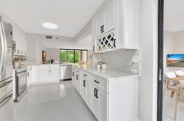 kitchen featuring light stone countertops, tasteful backsplash, kitchen peninsula, white cabinets, and appliances with stainless steel finishes