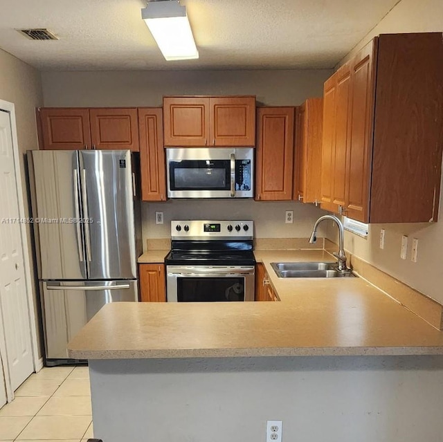 kitchen with kitchen peninsula, light tile patterned floors, sink, and appliances with stainless steel finishes