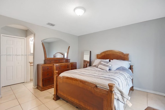 bedroom with light tile patterned floors, visible vents, arched walkways, and baseboards