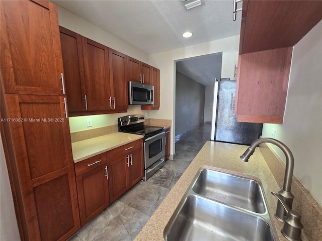 kitchen featuring light stone countertops, a textured ceiling, stainless steel appliances, and sink