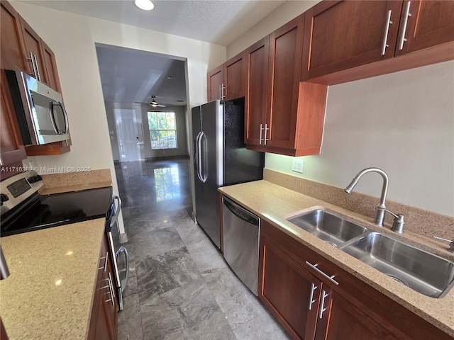 kitchen with light stone countertops, appliances with stainless steel finishes, ceiling fan, and sink