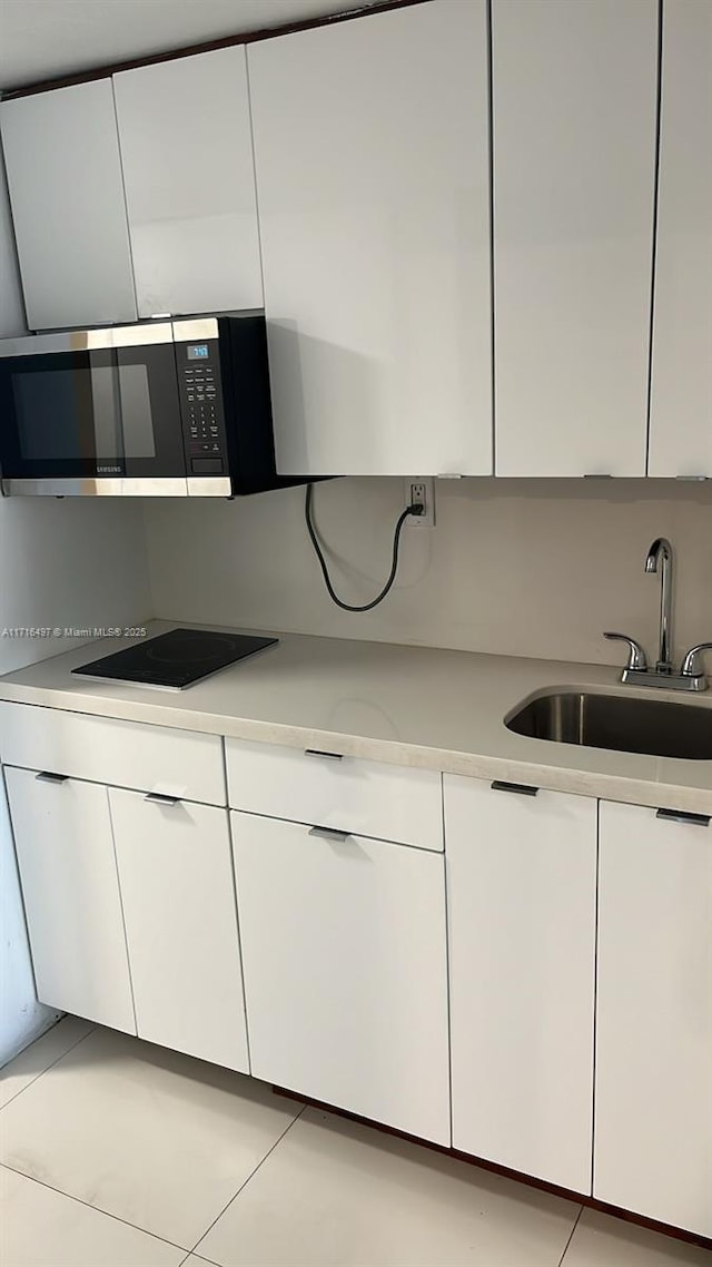 kitchen featuring light tile patterned floors, black electric cooktop, white cabinetry, and sink