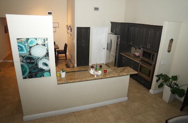 kitchen with light stone countertops, stainless steel appliances, kitchen peninsula, and light tile patterned flooring