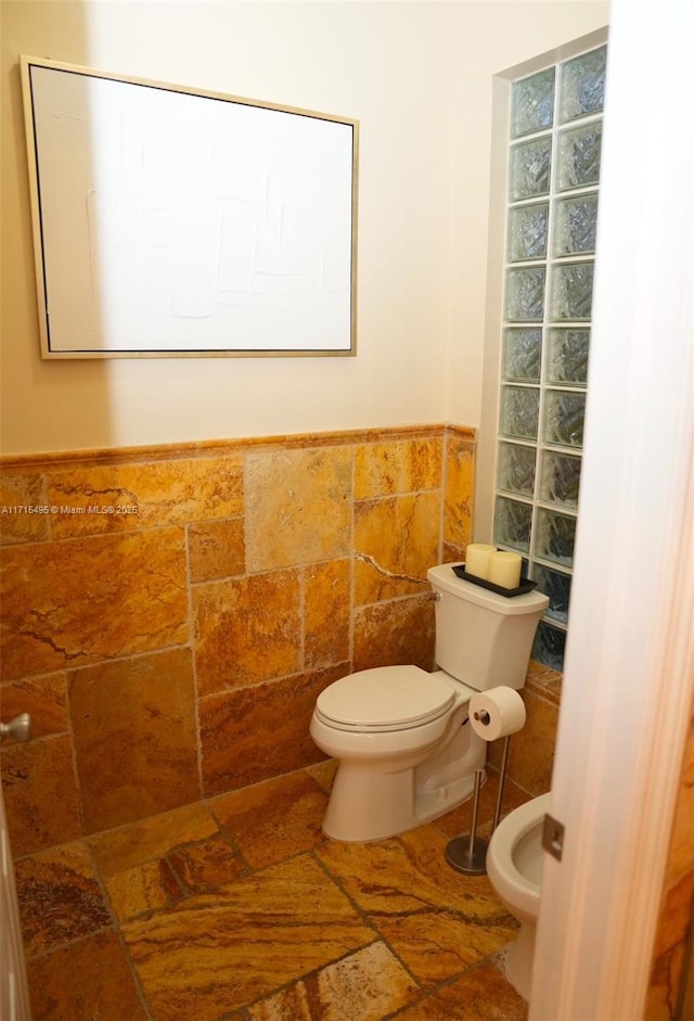 bathroom featuring a bidet, toilet, and tile walls