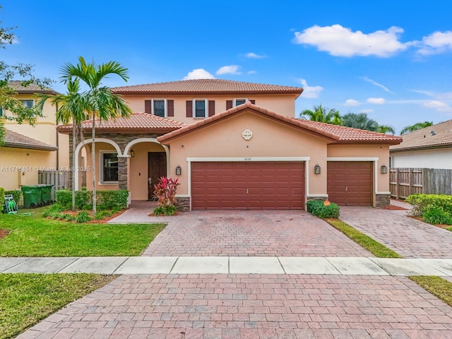 mediterranean / spanish-style home with decorative driveway, stucco siding, an attached garage, fence, and stone siding