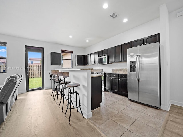 kitchen featuring visible vents, a kitchen island, appliances with stainless steel finishes, a breakfast bar, and recessed lighting