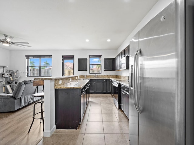 kitchen featuring light stone counters, stainless steel appliances, open floor plan, a kitchen island, and a kitchen breakfast bar