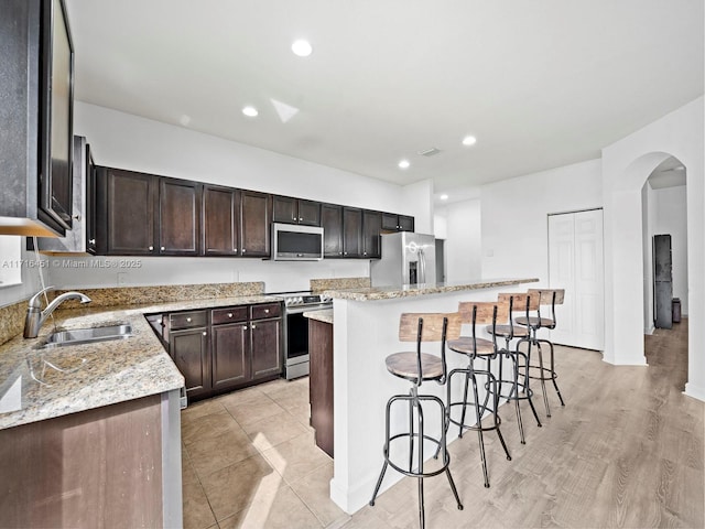 kitchen with light stone counters, a center island, a breakfast bar area, stainless steel appliances, and a sink