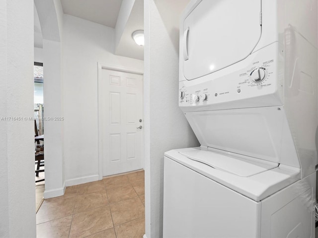 washroom featuring stacked washing maching and dryer, baseboards, light tile patterned floors, and laundry area