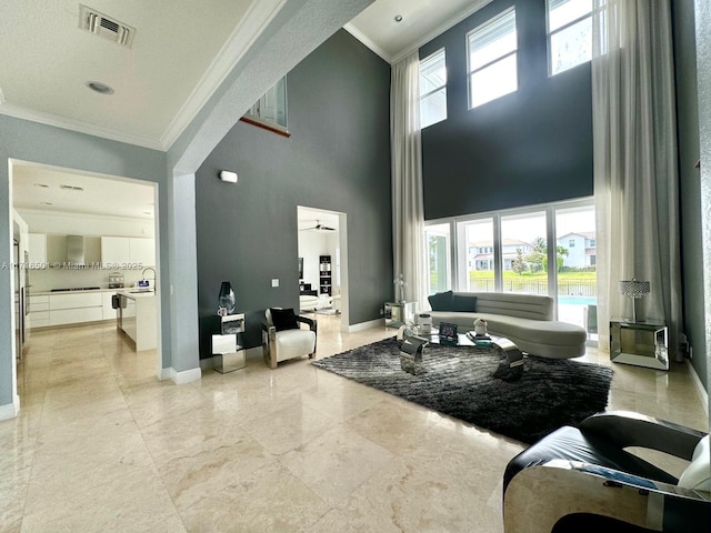 living room with a high ceiling, a wealth of natural light, ceiling fan, and crown molding