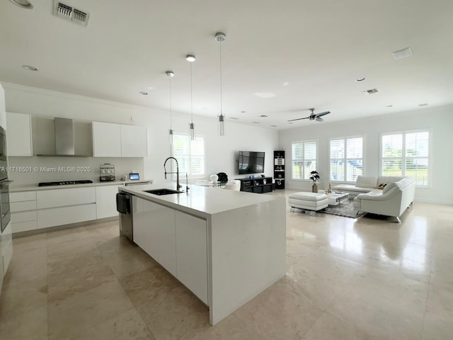 kitchen featuring sink, wall chimney exhaust hood, an island with sink, decorative light fixtures, and white cabinets