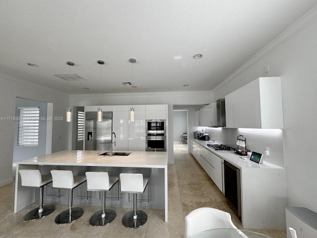 kitchen featuring white cabinets, a center island with sink, sink, hanging light fixtures, and built in appliances