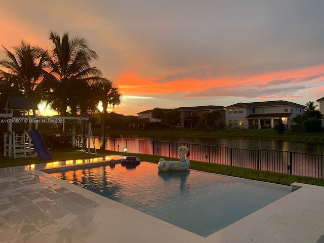 pool at dusk featuring a playground, a patio area, and a water view