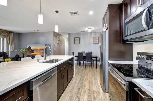 kitchen with dark brown cabinetry, stainless steel appliances, sink, light hardwood / wood-style flooring, and hanging light fixtures