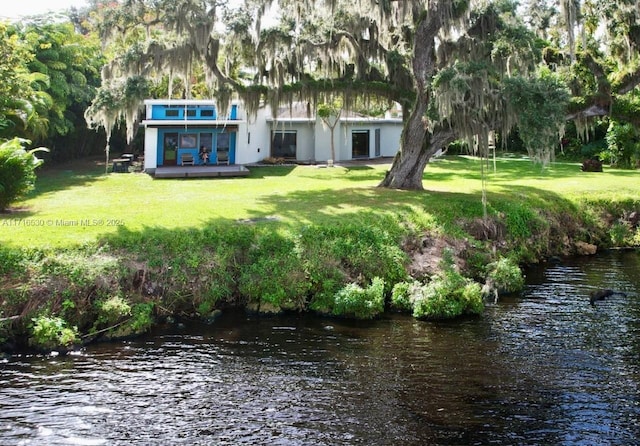 rear view of house with a deck with water view and a yard